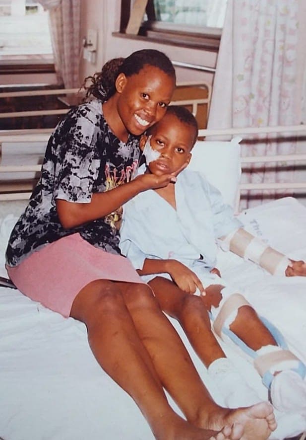 Jackson sitting up in a hospital bed with splints on one arm and one leg, beside a smiling family member.